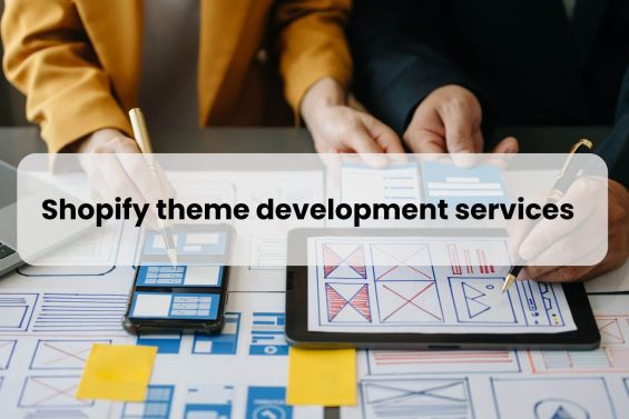 Image showing two professionals discussing over a tablet with digital wireframes and mobile devices on the table, with text overlay stating 'Shopify theme development services'. This represents a collaborative process in enhancing a Shopify store's design and functionality.